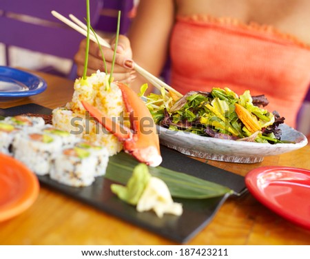 Close up of a Pretty Mixed Race Woman Enjoying A Meal At A Restaurant. African American female enjoying japanese cuisine at a fancy restaurant, using chopstick.