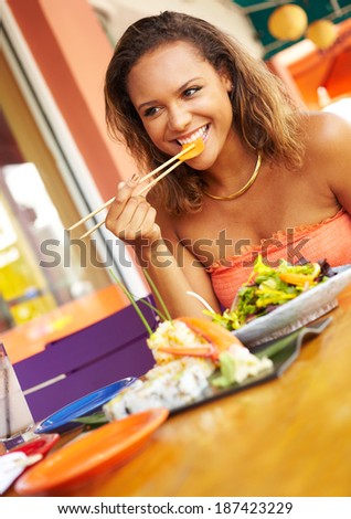Pretty Mixed Race Woman Enjoying A Meal At A Restaurant. African American female enjoying japanese cuisine at a fancy restaurant, using chopstick and really happy.