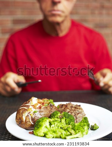 Midsection of senior man having strip steak served with loaded baked potato and broccoli at restaurant table
