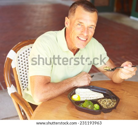 Portrait of happy mature man eating baked tilapia served with broccoli and wild rice at restaurant