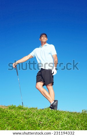 Full length of mature male golfer standing with club on course against clear blue sky