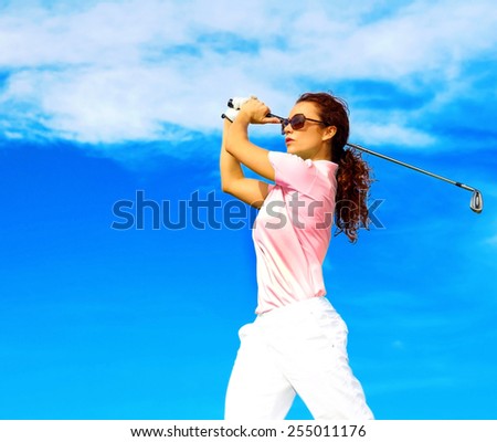 Low angle view of confident young woman swinging golf club against blue sky