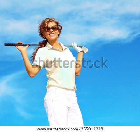 Low angle view of smiling woman holding golf club on shoulders against blue sky