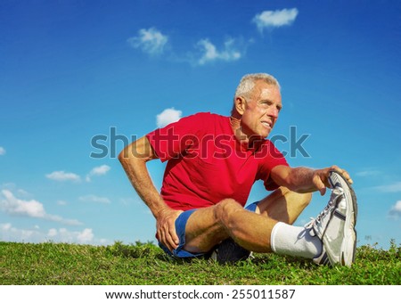 Full length of senior man in pain while stretching leg on meadow