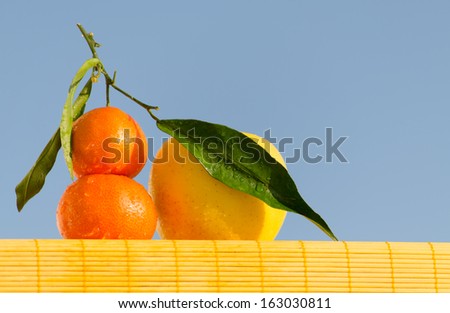 Tangerines and an apple in water drops standing on a yellow bamboo mat in front of the blue sky