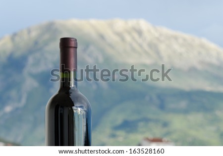 A closeup of a red wine bottle neck in front of a mountain