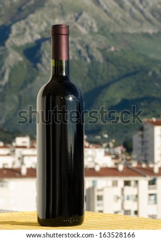 A closeup shot of a red wine bottle with no label on outside in natural light in front of a mountain