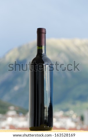 Red wine bottle with no label on outside in front of a blurry mountain and a town