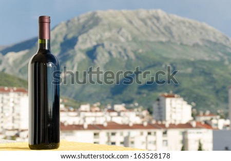 Red wine bottle with no label on outside in natural light in front of a mountain city