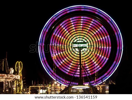 Pink and yellow ferris wheel against black background and carnival lights
