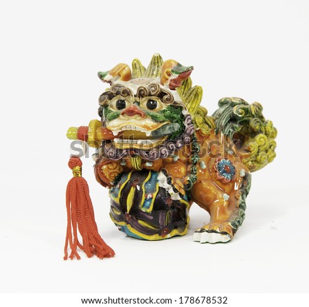 Ceramic multicolored Chinese lion with red tasseled sword in its mouth against a white background