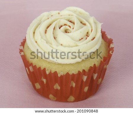 Homemade vanilla cupcake with vanilla swirled icing and red sugar in a red and white cupcake paper against a pink background