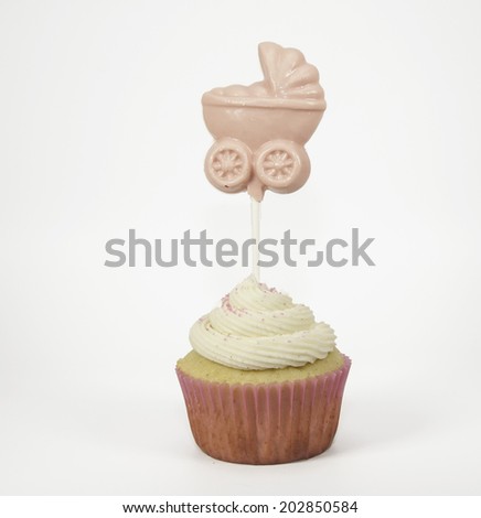 It\'s a Girl homemade vanilla cupcake and buttercream icing in a pink cupcake paper and pink baby carriage lollipop against a white background