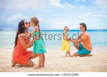 Mom with her older daughter in the foreground and dad with youngest daughter in the background on the beach