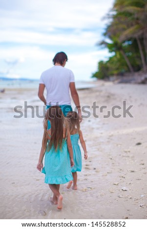 Back view of father and his two little daughters walking by the sea