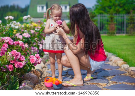 Young mother with her beautiful daughter sniffing flowers in the garden