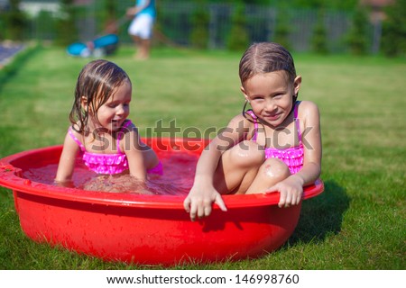 Two cute little sisters frolicing and splashing in their yard in small pool