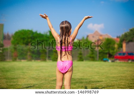 Back view of little girl in a swimsuit playing and splashing in the yard
