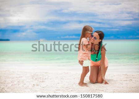 Young mother and her cute little girl whispering on the white beach