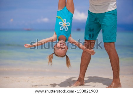 Father holding his happy smiling daughter upside down on sandy beach