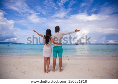 Back view of young couple spread their arms standing on white sandy beach