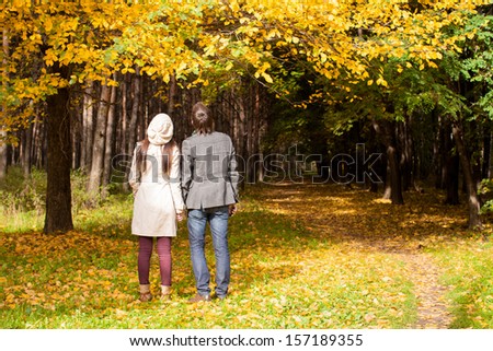 Back view of Young couple in love on the big autumn meadow under large maple tree at sunny fall day