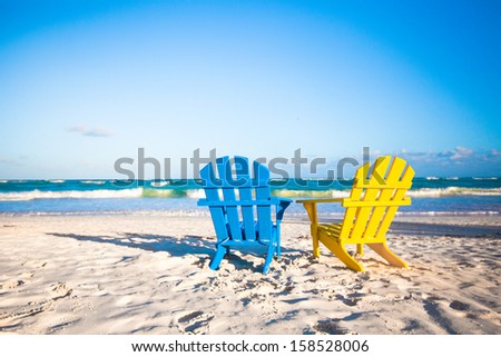 Two wooden chairs: yellow and blue on a white sandy beach, Mexico