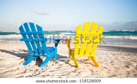 Two wooden chairs: yellow and blue on a white sandy beach, Mexico