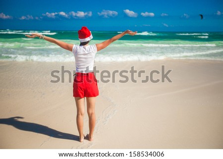 Back view of young woman in Santa Hat walking spread her hands on white beach