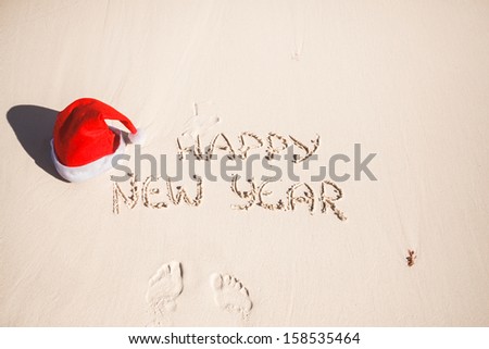 Happy New Year written in the sand and Santa Hat on white sandy beach