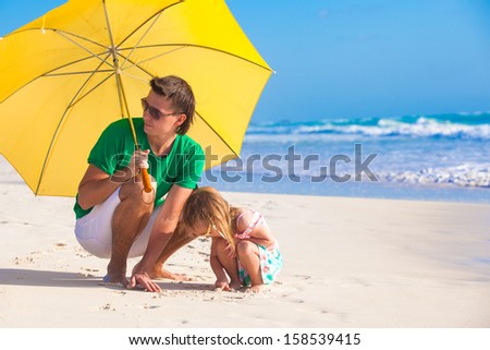 Young father and his adorable little daughter hiding from the sun under a yellow umbrella on white sunny day