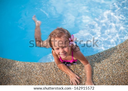 Little cute happy girl with flower behind her ear has fun in the swimming pool