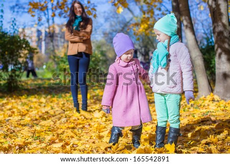 Two beautiful adorable daughter walking with his young mom in the park on a sunny autumn day