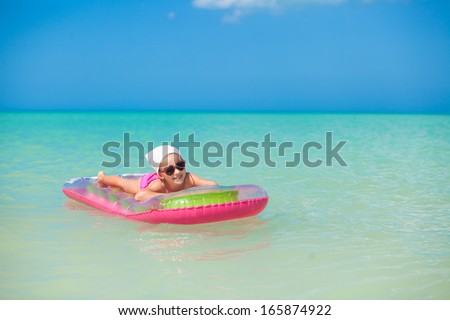 Little cute girl sunbathing on pink air-bed in warm sea