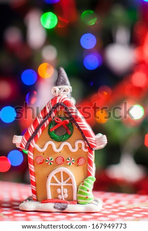 Gingerbread fairy house decorated by colorful candies on a background of bright Christmas tree with garland