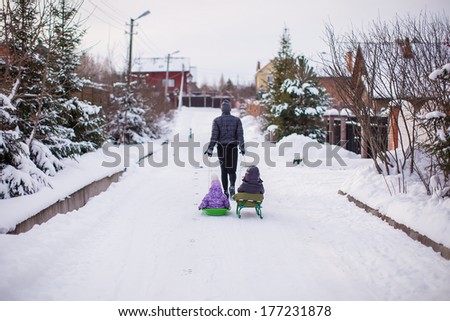 Young father rolls his little cute daughters on a sled in the snow outdoors