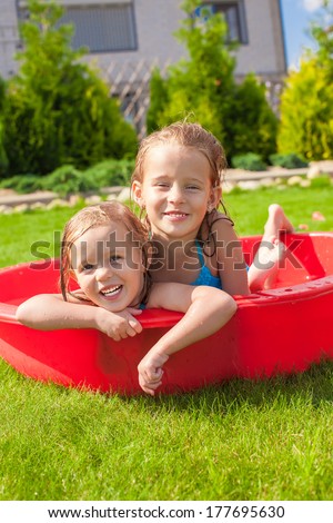 Two Little Happy Girls Having Fun In Small Pool Outdoor On Summer Day