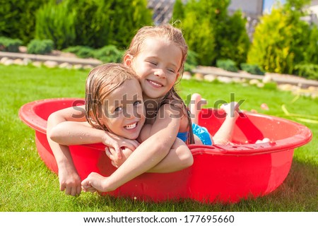 Two adorable little happy girls having fun in small pool outdoor on summer day