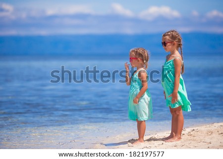 Little adorable girls in turquoise dress on white beach look at the sea