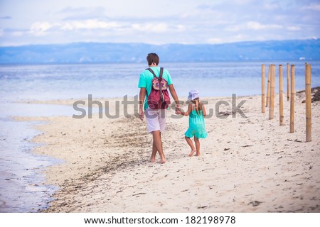 Back view of young father and his little girl walking by the sea