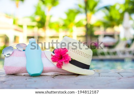 Suncream, hat, sunglasses, flower and tower near swimming pool