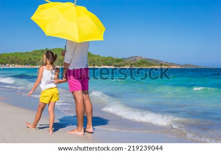 Back view of father and daughter at white beach with yellow umbrella