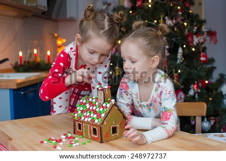 Little adorable girls decorating gingerbread house for Christmas