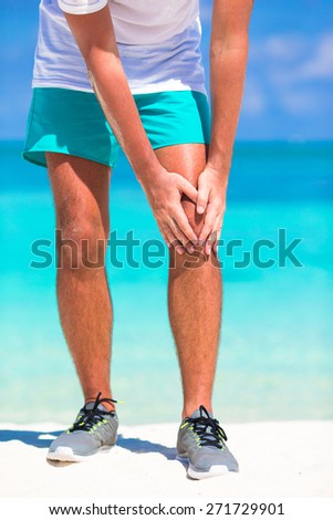 Male athlete suffering from pain in leg while exercising on white beach
