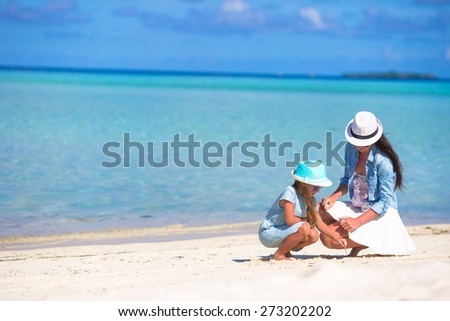 Mother and baby girl drawing on sandy beach