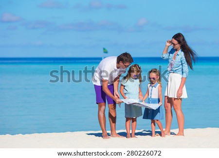 Happy young family of four with map on the beach
