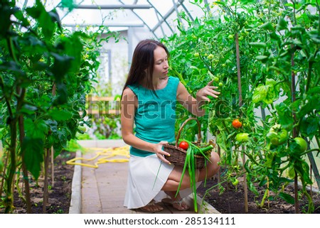 Young woman holding a basket of greenery and vegetables in the greenhouse