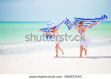 Little girls having fun running with towels on tropical beach