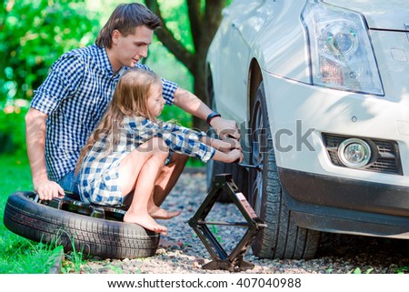 Adorable little girl sitting on a tire and helping father to change a car wheel outdoors on beautiful summer day