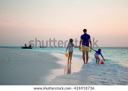 Father and kids walking on white sandy beach